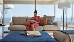 Femme relaxante avec tablette numérique sur canapé vitrine maison de luxe — Photo de stock