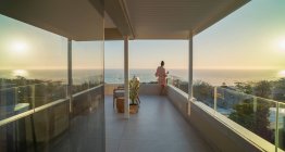 Жінка відпочиває на сонячному балконі з видом на океан заходу сонця — стокове фото