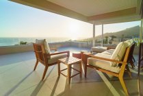 Sofa and armchair on sunny tranquil luxury patio with ocean view — Stock Photo