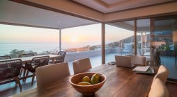 Ordinateur portable sur table à manger de luxe avec vue panoramique sur l'océan au coucher du soleil — Photo de stock