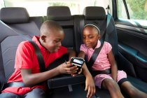 Брат і сестра використовують смартфон на задньому сидінні автомобіля — стокове фото