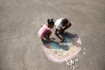 Brother and sister drawing rainbow with sidewalk chalk on pavement — Stock Photo