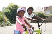 Retrato feliz hermano y hermana montando bicicletas en el barrio soleado - foto de stock