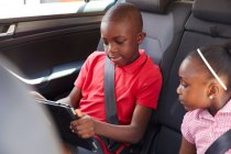 Брат і сестра використовують цифровий планшет на задньому сидінні автомобіля — стокове фото