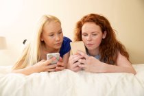Preteen menina amigos usando telefones inteligentes na cama — Fotografia de Stock