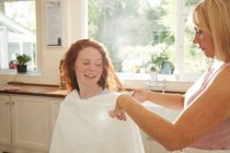 Мати ріже волосся для дев'ятнадцяти доньки на сонячній кухні — стокове фото