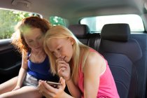 Preteen girls friends using smartphone in back seat of car — Stockfoto