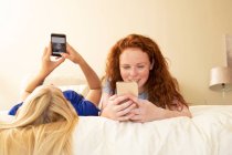 Amigos preadolescentes usando teléfonos inteligentes en la cama - foto de stock