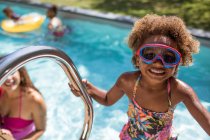 Portrait cute girl in swimming goggles at sunny swimming pool — Stock Photo
