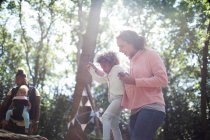 Mutter hilft Tochter beim Balancieren auf umgestürztem Baumstamm im sonnigen Wald — Stockfoto