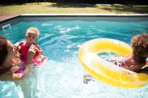 Madre e hijas jugando en la soleada piscina de verano - foto de stock