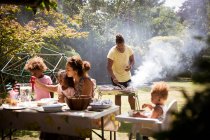 Barbecuant et mangeant en famille sur le patio ensoleillé de l'arrière-cour d'été — Photo de stock