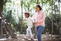 Mother helping daughter walk on fallen log in sunny woods — Stock Photo