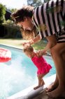 Mother helping curious toddler daughter at edge of swimming pool — Stock Photo