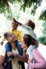 Genitori felici che portano figlie sulle spalle sotto gli alberi nel parco — Foto stock