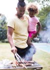 Padre che tiene figlia alla griglia nel cortile estivo — Foto stock