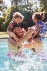 Pais e filhas brincalhões jogando frango na piscina ensolarada — Fotografia de Stock