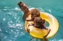 Father and daughters in inflatable ring in sunny summer swimming pool — Stock Photo