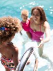 Mother watching daughter get into sunny summer swimming pool — Stock Photo