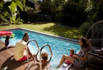 Felice famiglia rilassante a soleggiata estate patio a bordo piscina — Foto stock