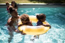 Сім'я грає з надувним кільцем у сонячному літньому басейні — стокове фото