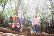 Familie spielt auf umgestürzten Baumstämmen unter Bäumen im sonnigen Sommerwald — Stockfoto
