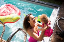 Счастливая мать поднимает дочь в солнечный летний бассейн — стоковое фото
