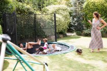 Famiglia che gioca sul trampolino soleggiato del cortile — Foto stock