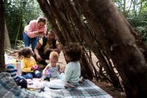 Familia feliz jugando al té en el fuerte del árbol en el bosque - foto de stock