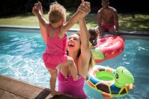 Playful mother lifting toddler daughter into sunny swimming pool — Stock Photo