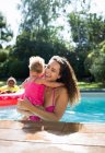 Happy mother holding daughter in sunny summer swimming pool — Stock Photo