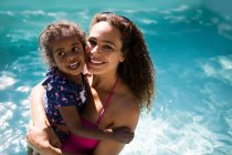 Portrait happy mother and daughter in sunny summer swimming pool — Stock Photo