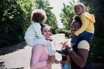 Porträt glückliches Paar trägt Töchter auf Schultern auf sonniger Straße — Stockfoto