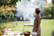 Woman barbecuing and watching family play on backyard trampoline — Stock Photo