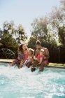 Familia feliz chapoteando en la soleada piscina de verano - foto de stock