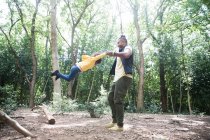 Pai brincalhão balançando filha abaixo de árvores em bosques ensolarados — Fotografia de Stock