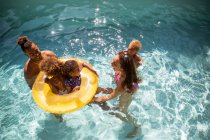 Счастливая семья играет на надувном кольце в солнечном летнем бассейне — стоковое фото