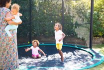 Feliz madre e hijas jugando en el soleado trampolín patio trasero - foto de stock