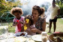 Mãe e filhas desfrutando de churrasco almoço na mesa do quintal — Fotografia de Stock