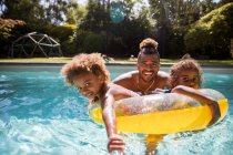 Retrato feliz pai e filhas brincando na piscina ensolarada — Fotografia de Stock