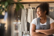 Smiling female shop owner looking away with arms crossed — Stock Photo