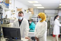 Cientistas em máscaras faciais trabalhando no computador em laboratório — Fotografia de Stock
