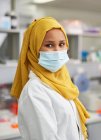 Ritratto scienziata donna sicura di sé in hijab e maschera facciale in laboratorio — Foto stock