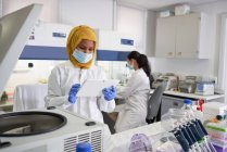 Cientista feminina em máscara facial e hijab usando comprimido digital em laboratório — Fotografia de Stock