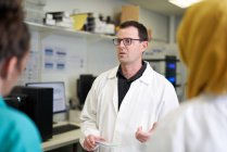 Мужчина-ученый беседует с коллегами в лаборатории — стоковое фото