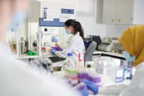 Женщина-ученый в маске для лица и перчатках работает в лаборатории — стоковое фото