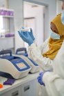 Female scientist in hijab and gloves examining specimen tray — Stock Photo
