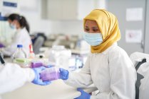Женщина-ученый в хиджабе в маске для лица работает в лаборатории — стоковое фото