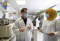 Científicos en máscaras faciales hablando en laboratorio - foto de stock