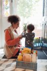 Baby daughter helping mother unload grocery delivery at front door — Stock Photo